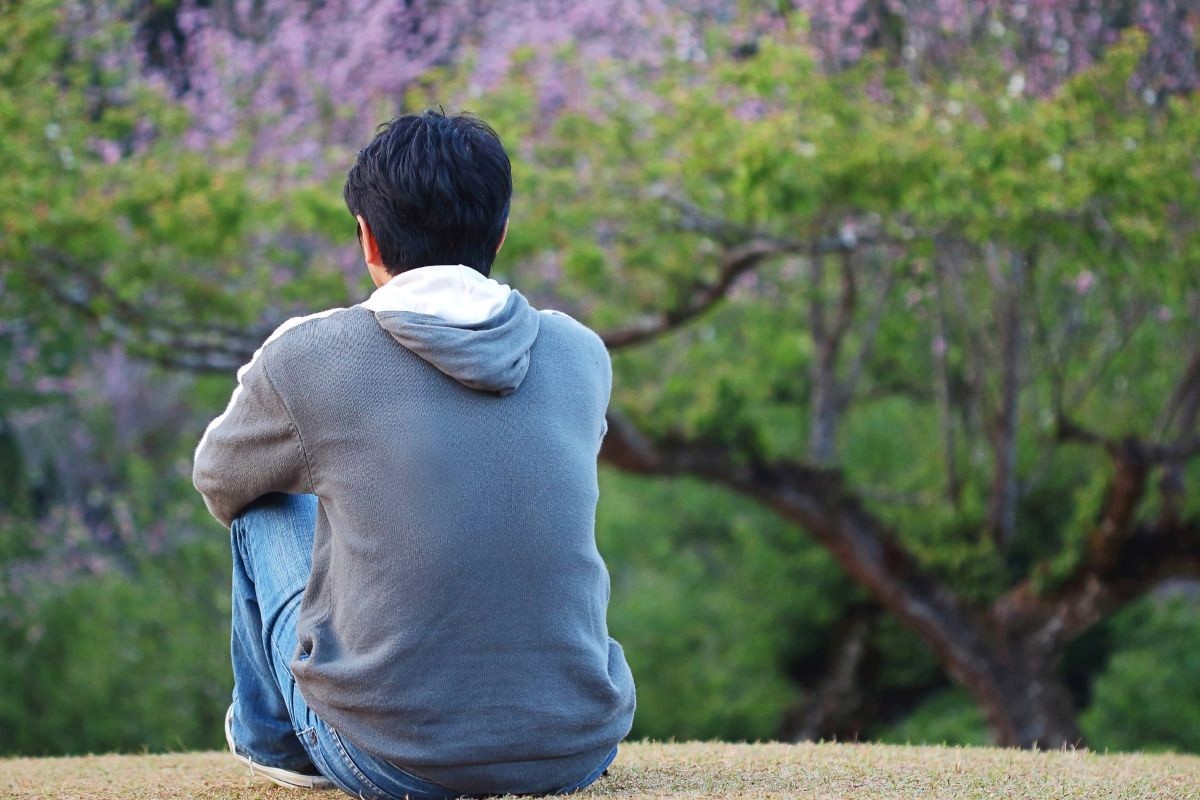 un homme assis de dos dans la nature qui regarde au loin