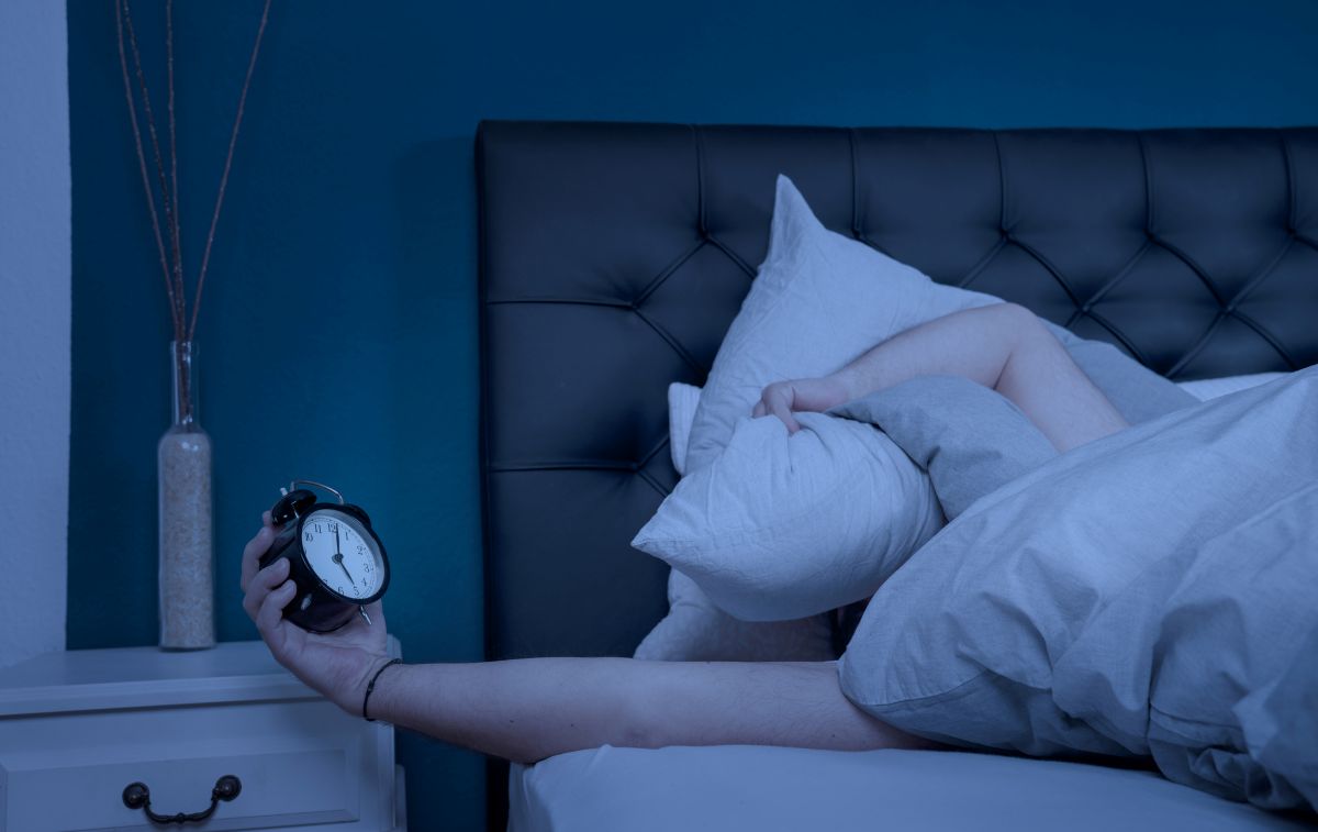 un homme allongé qui tient son réveil dans sa main