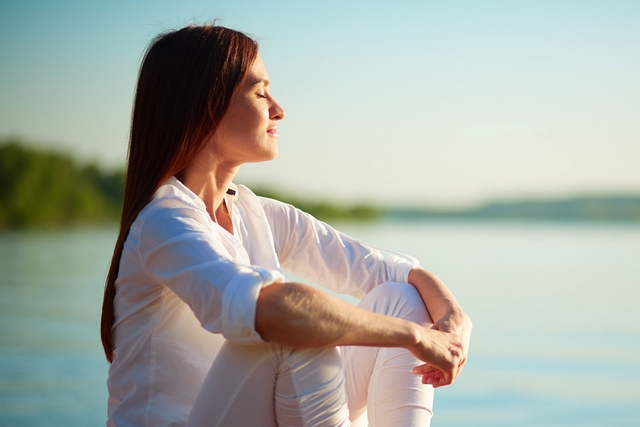 femme assise au bord de l'eau les yeux fermes